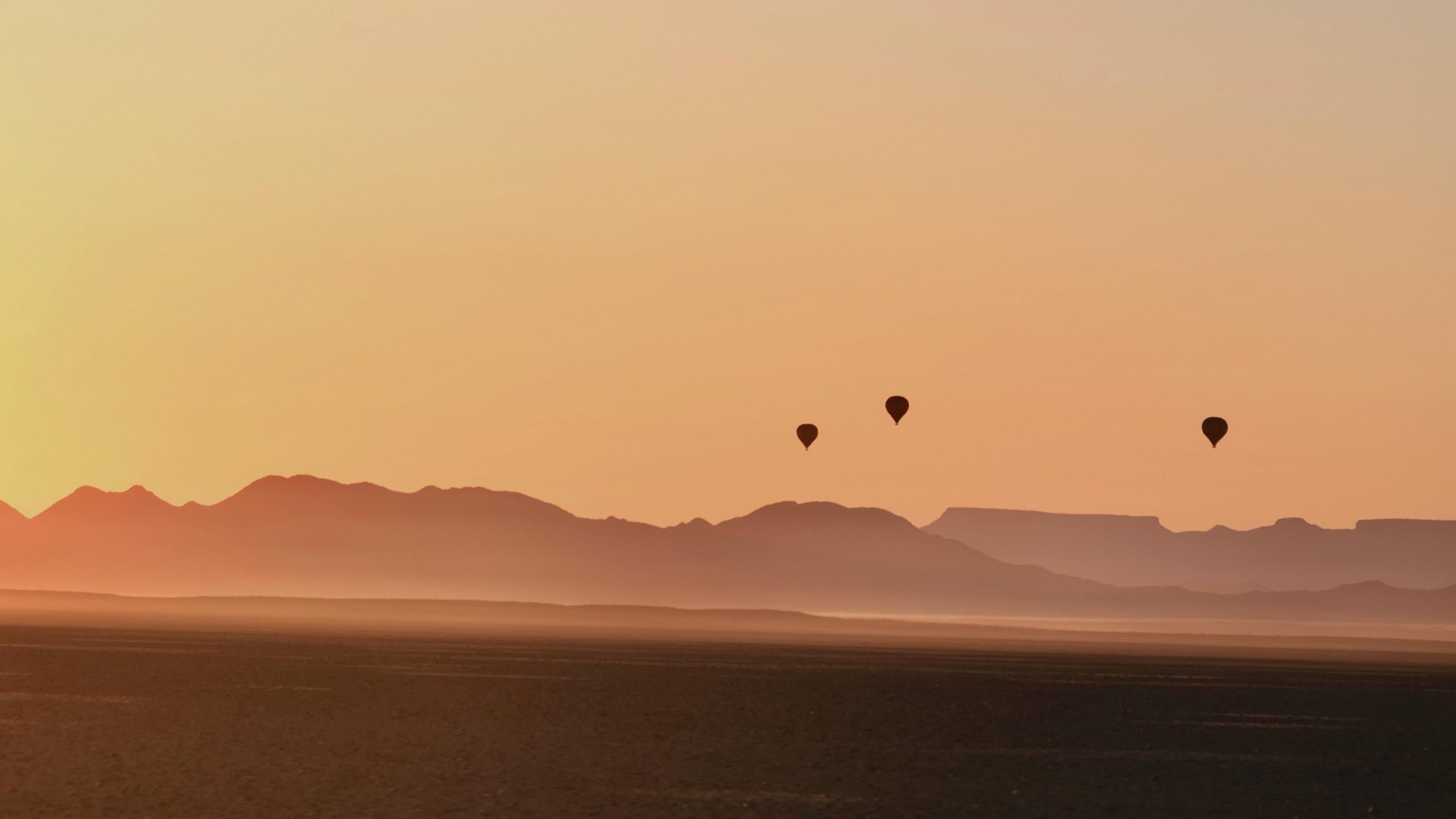 Sunrise or sunset over a desert with mountains and hot air balloons in the distance.